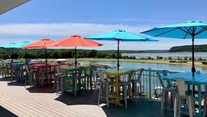 Una terraza con mesas y sillas al aire libre, sombrillas y vistas a un lago.