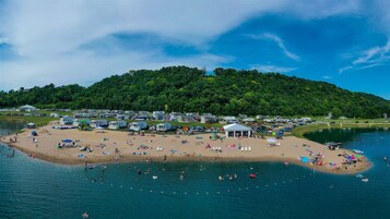 Uma praia às margens do lago, com veículos recreativos, um gazebo e uma colina arborizada.