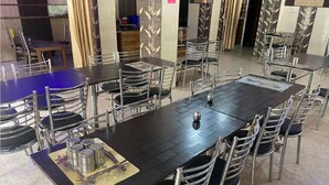 A dining area with multiple tables and chairs, a central table with a decorative item, and a blue table in the background. - Raj Palace (Joshimath)