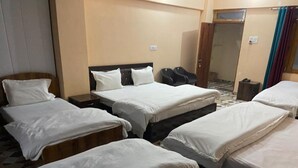 A hotel room with multiple beds, a wooden headboard, a small table, and a door leading to a bathroom. - Raj Palace (Joshimath)