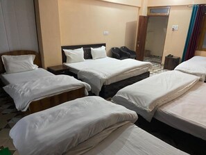 Quarto de hotel com várias camas, cabeceira de madeira, uma pequena mesa e porta que dá para um banheiro.