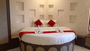 A hotel room with a round bed, two red pillows, a white bedspread, and a mirror on the wall. - Shagun Resort & Water Park (Igatpuri)