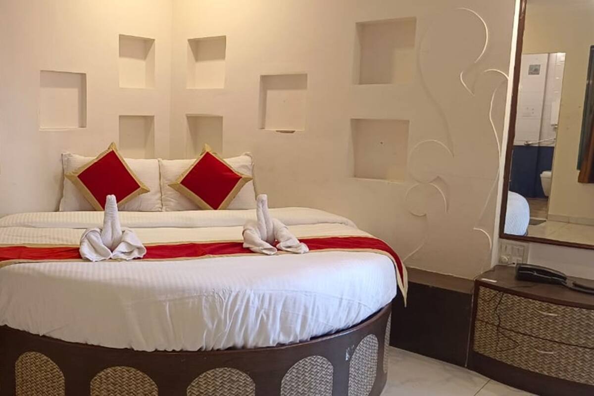 Een hotelkamer met een rond bed, twee rode kussens, een witte dekbedovertrek en een spiegel aan de muur.
