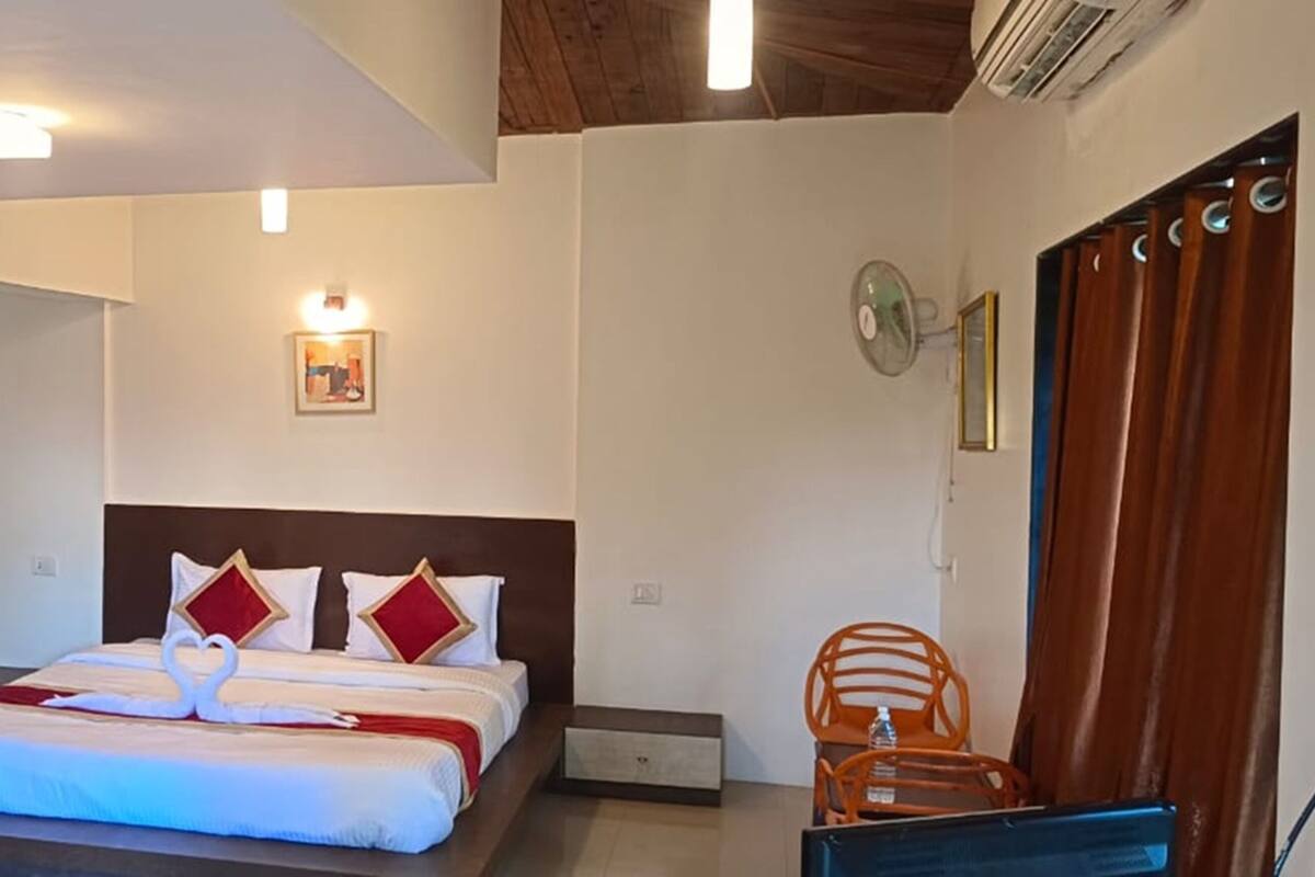 Een hotelkamer met een bed, een bureau, een stoel, een ventilator en een foto aan de muur.
