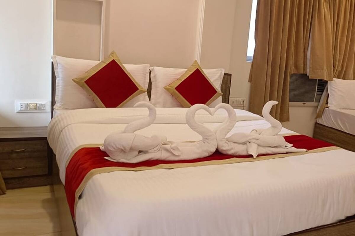 Een hotelkamer met een bed, nachtkastje, raam met gordijnen en een klein tafeltje met een handdoek.