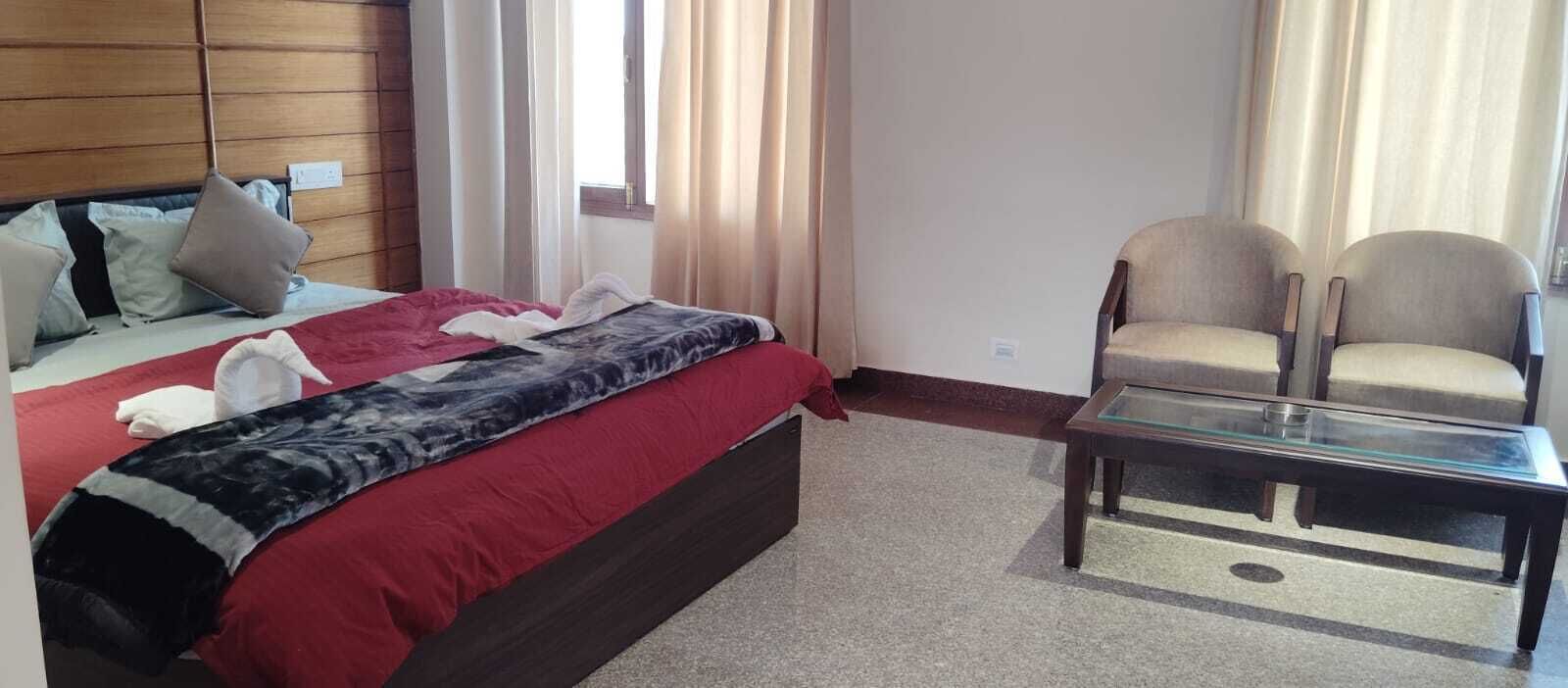 Una camera d'albergo con un letto, due sedie, un tavolino in vetro e una finestra con tende.
