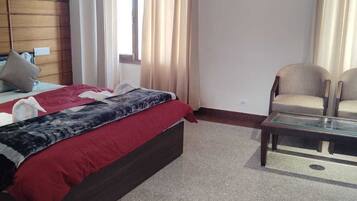 Una camera d'albergo con un letto, due sedie, un tavolino in vetro e una finestra con tende.
