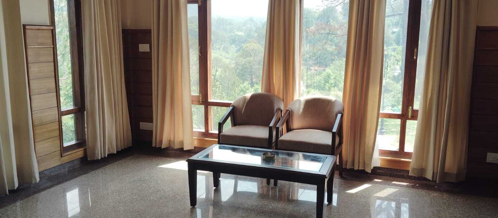 A room with a glass coffee table, two armchairs, and large windows with curtains.