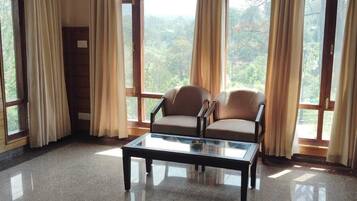 A room with a glass coffee table, two armchairs, and large windows with curtains.