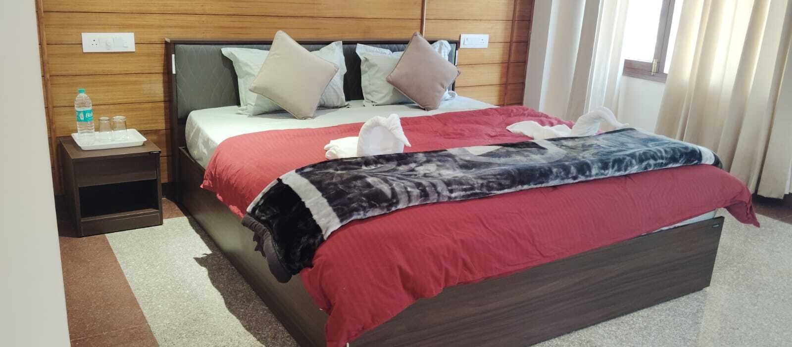 A hotel room with a bed, pillows, a nightstand with a water bottle, and a red blanket.