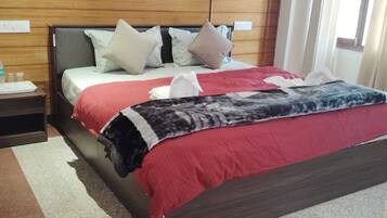 A hotel room with a bed, pillows, a nightstand with a water bottle, and a red blanket.