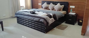 A bedroom with a bed, nightstands, a wooden headboard, and a small table with a bottle and glasses. - Hotel Som Kunj Circuit House (Palampur)