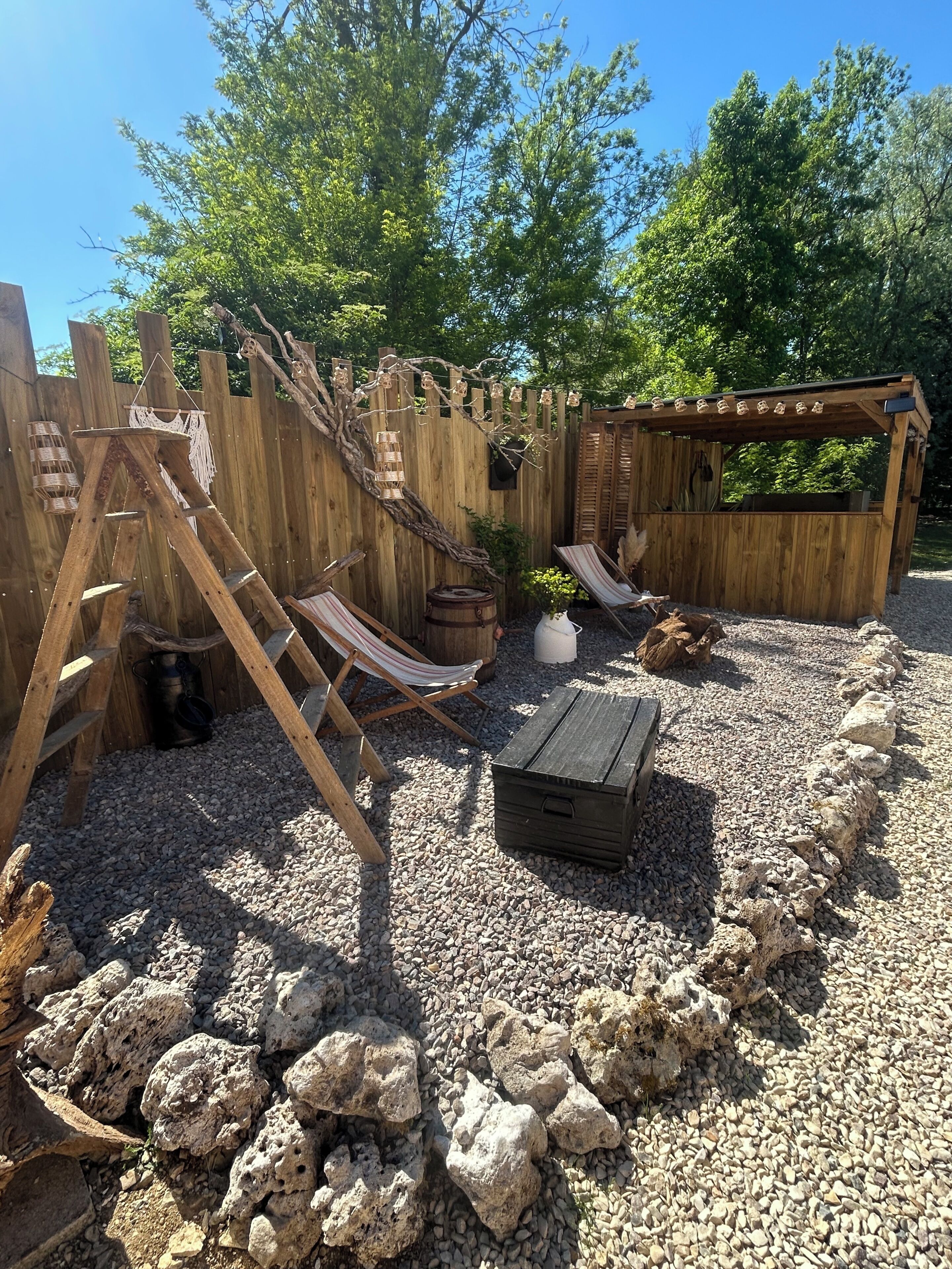 A wooden play structure with slides and a ladder, surrounded by gravel and rocks.