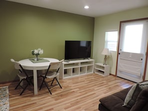 Una sala de estar con una mesa de comedor, sillas, un televisor de pantalla plana, una lámpara y un sofá.