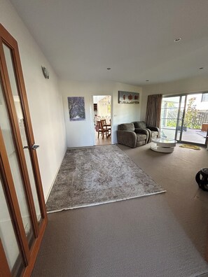 A spacious living room with a large rug, a sofa, and a dining area in the background.