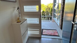 A hallway with a white cabinet, a framed picture, and a door leading to a balcony with a view of greenery. - House is near to university, AIS, mountain, lake and CBD. Family - friendly. (Bruce)