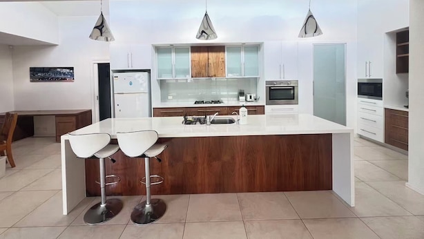 A modern kitchen with a central island, white cabinetry, and pendant lighting. - House is near to university, AIS, mountain, lake and CBD. Family - friendly. (Bruce)