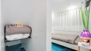 Et værelse med en seng, en hylde med puder, et vindue med gardiner og en blå gulv.