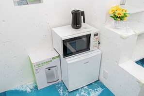 Una cocina compacta equipada con microondas, un refrigerador pequeño y una caja con la etiqueta 'Lunino E-200'.