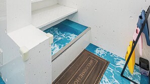 Et badeværelse med en hvid vask, et spejl, et lille vindue og et bruseområde med blå fliser.
