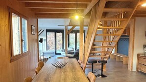 Ein Holzinterieur mit einem langen Esstisch, Stühlen, einer Treppe und Blick durch eine Glastür.