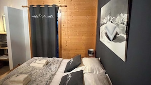 Ein Schlafzimmer mit Holzbalkendecke, einem Bett mit weißer und schwarzer Bettwäsche, einem Bild an der Wand und einem Vorhang mit Bergmotiv.