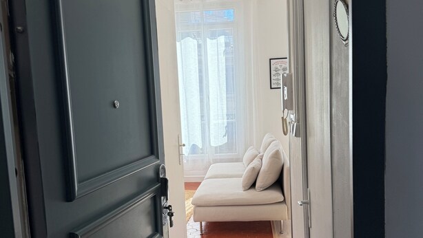 A hallway leading to a bedroom with a bed, a door, and a window with curtains. - Charming, cosy apartment in the Antique Quarter (Marseille)