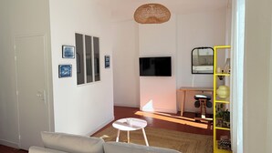 A living room with a sofa, a small round table, a TV, and a yellow shelving unit with plants. - Charming, cosy apartment in the Antique Quarter (Marseille)