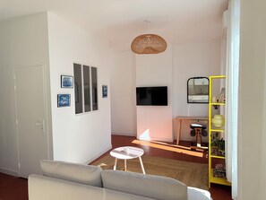 A living room with a sofa, a small round table, a TV, and a yellow shelving unit with plants. - Charming, cosy apartment in the Antique Quarter (Marseille)