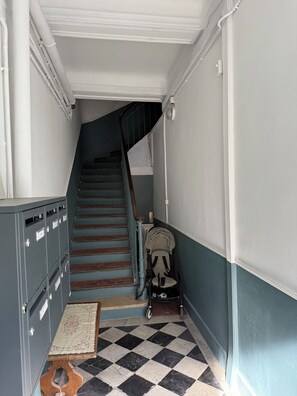 A narrow hallway with a checkered floor, a staircase, and a baby stroller. - Charming, cosy apartment in the Antique Quarter (Marseille)