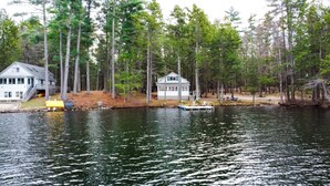 Una cabaña junto al lago con un muelle, rodeada de altos árboles.