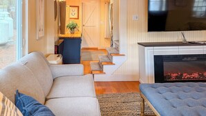 Una sala de estar con sofá, televisor, chimenea y una escalera que lleva a otra habitación.