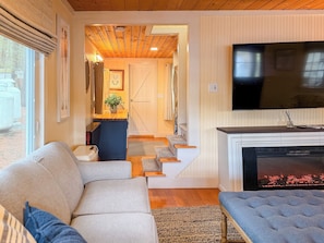 A living room with a sofa, a television, a fireplace, and a staircase leading to another room. - Lakefront Cabin - Private Dock, Hot Tub & Fire Pit (Barrington)