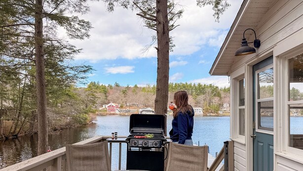 Una terraza con una parrilla, una mesa de vidrio y vistas a un lago y casas.