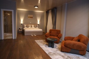 Een hotelkamer met een bed, een zithoek met een stoel en een tafeltje, een nachtkastje en een wandlamp.