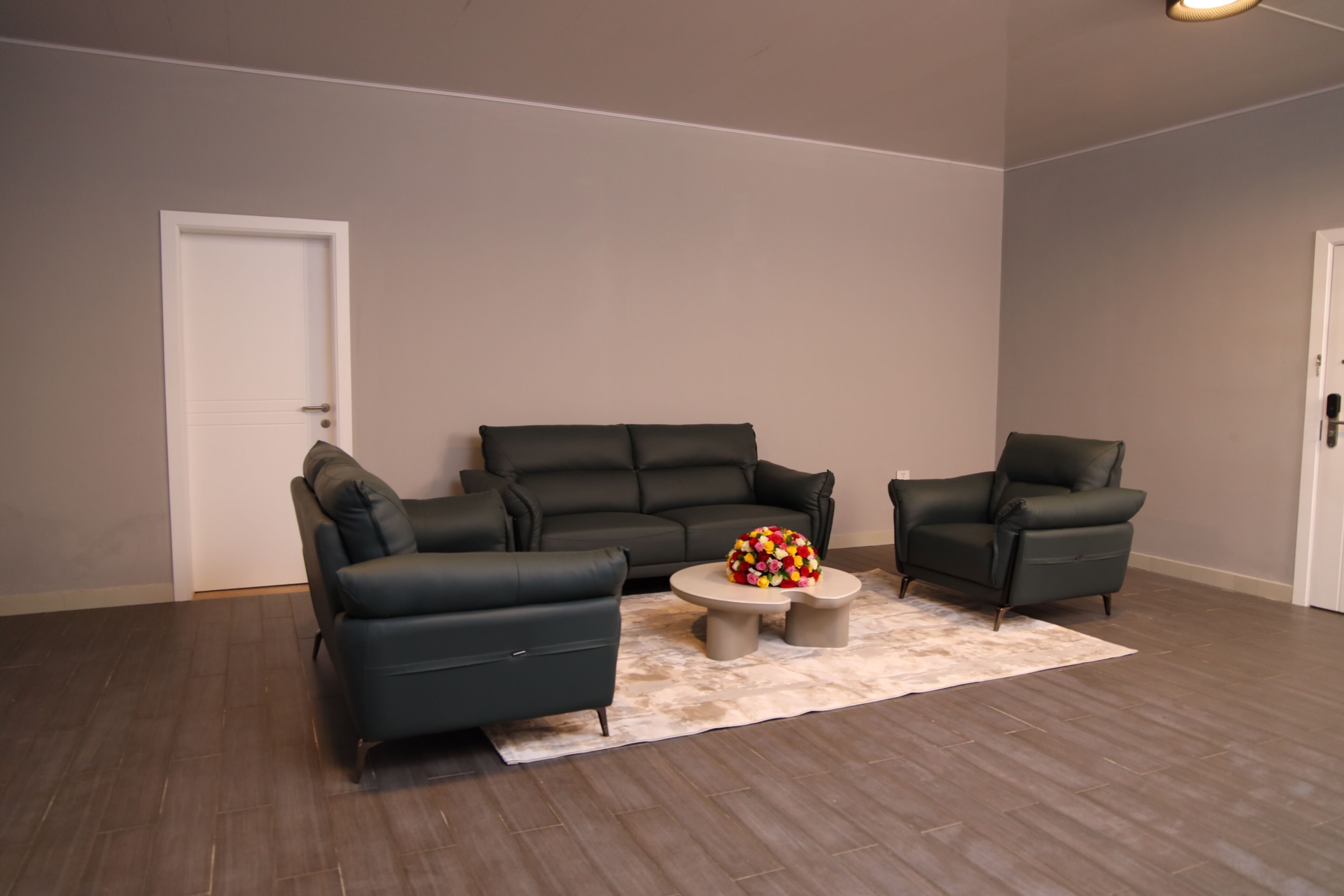 Uma sala de estar com um sofá de couro escuro, uma poltrona combinando, uma mesa de centro e um tapete.
