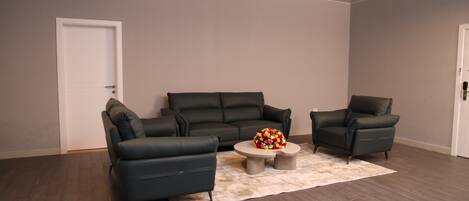 Uma sala de estar com um sofá de couro escuro, uma poltrona combinando, uma mesa de centro e um tapete.