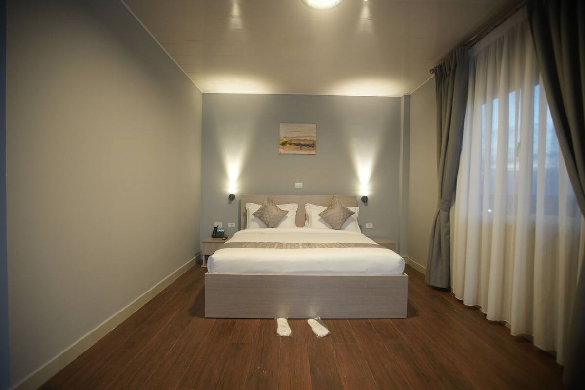 A bedroom with a large bed, two bedside tables, a nightstand, and a painting on the wall.