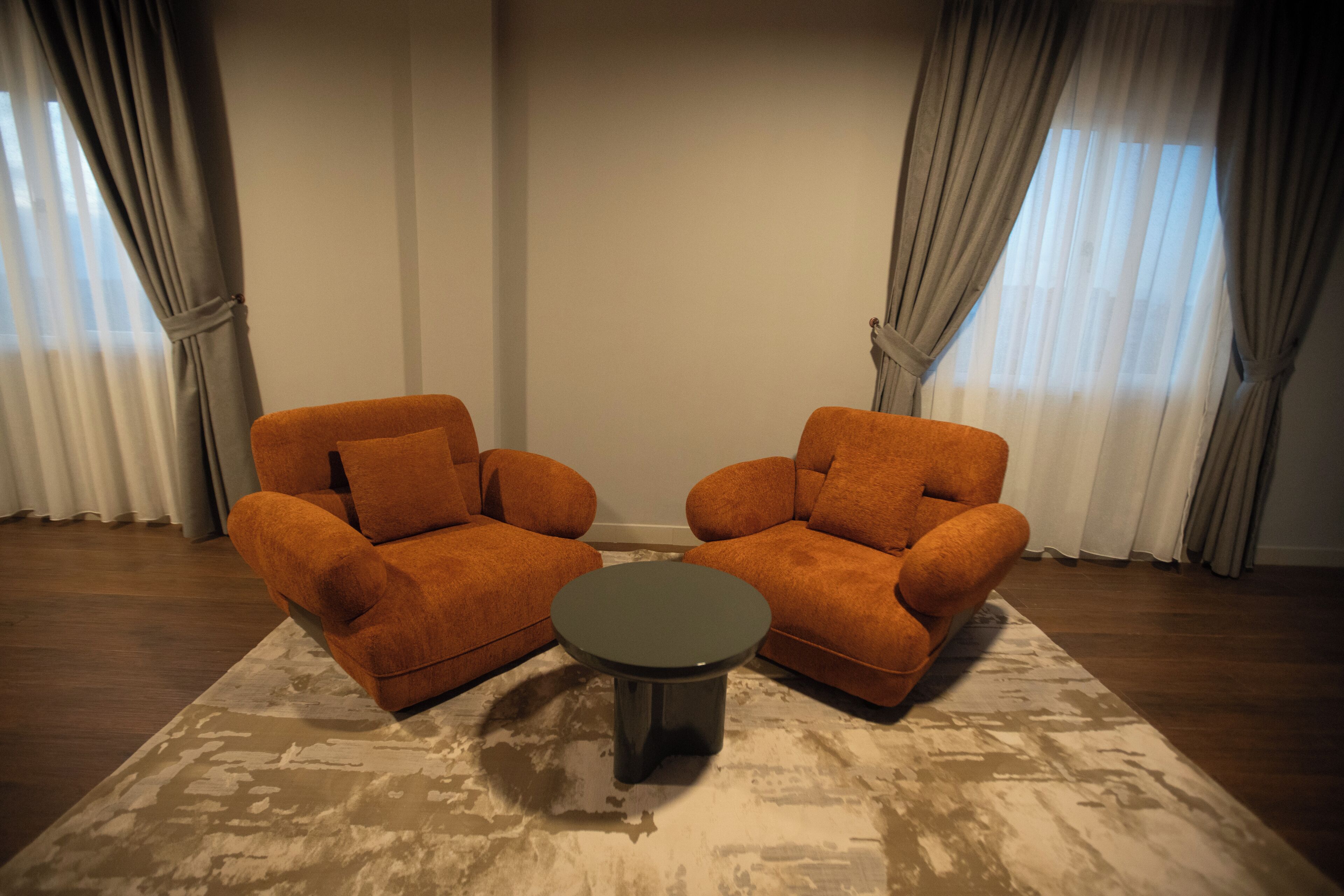 A room with two orange armchairs, a small round table, and a patterned rug.