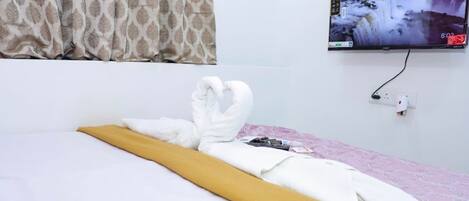 A hotel room with a bed, a television mounted on the wall, and a window with patterned curtains.
