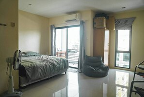 A bedroom with a bed, a standing fan, a bean bag chair, and a sliding glass door leading to a balcony. - Room-cozy Old Town Room 5 min Walk Local (Phuket)