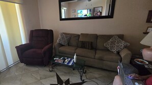 A living room with a red armchair, a sofa with patterned cushions, a coffee table with magazines, and a laptop on the sofa. - Cozy 1-bedroom condo in fantastic San José del Cabo with AC. Close to the beach (San José del Cabo)