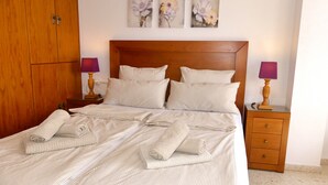 Siististi pedattu sänky, jossa on raidallinen vuodevaatesetti, puinen pääty ja kaksi yöpöytää, joissa on lamput.