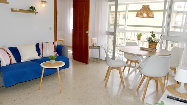 Een woonkamer met een blauwe bank, een klein rond tafeltje en een eethoek met een witte tafel en stoelen.