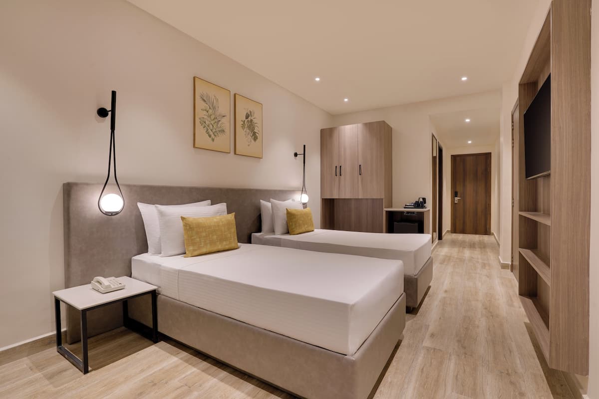 Una habitación de hotel con dos camas, una mesita de noche con teléfono, una lámpara de pared y un armario.