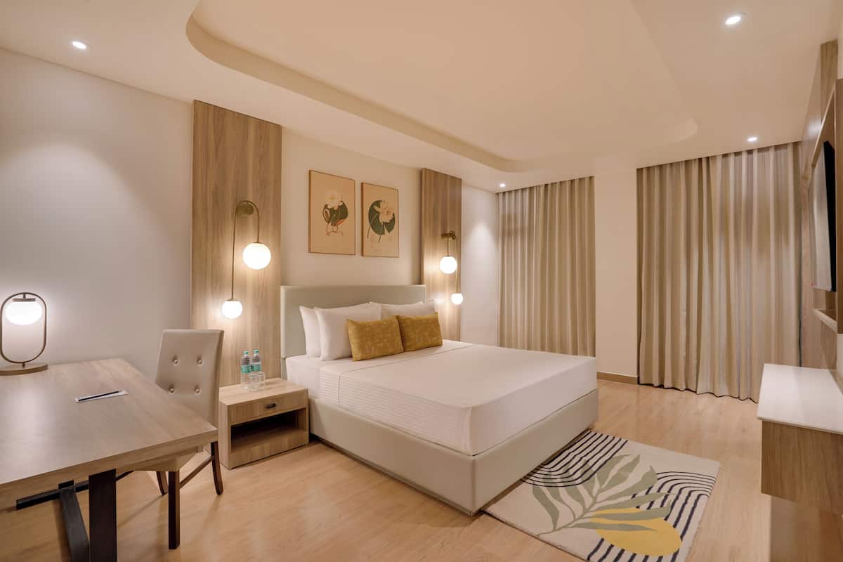 Una habitación de hotel moderna con cama, mesitas de noche, escritorio y un ventanal con cortinas.