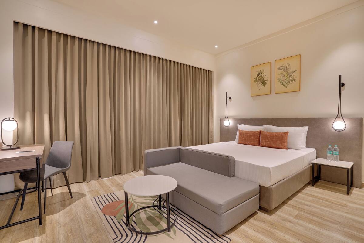 Una habitación de hotel moderna con cama, escritorio, silla, una mesita pequeña y mesita de noche.