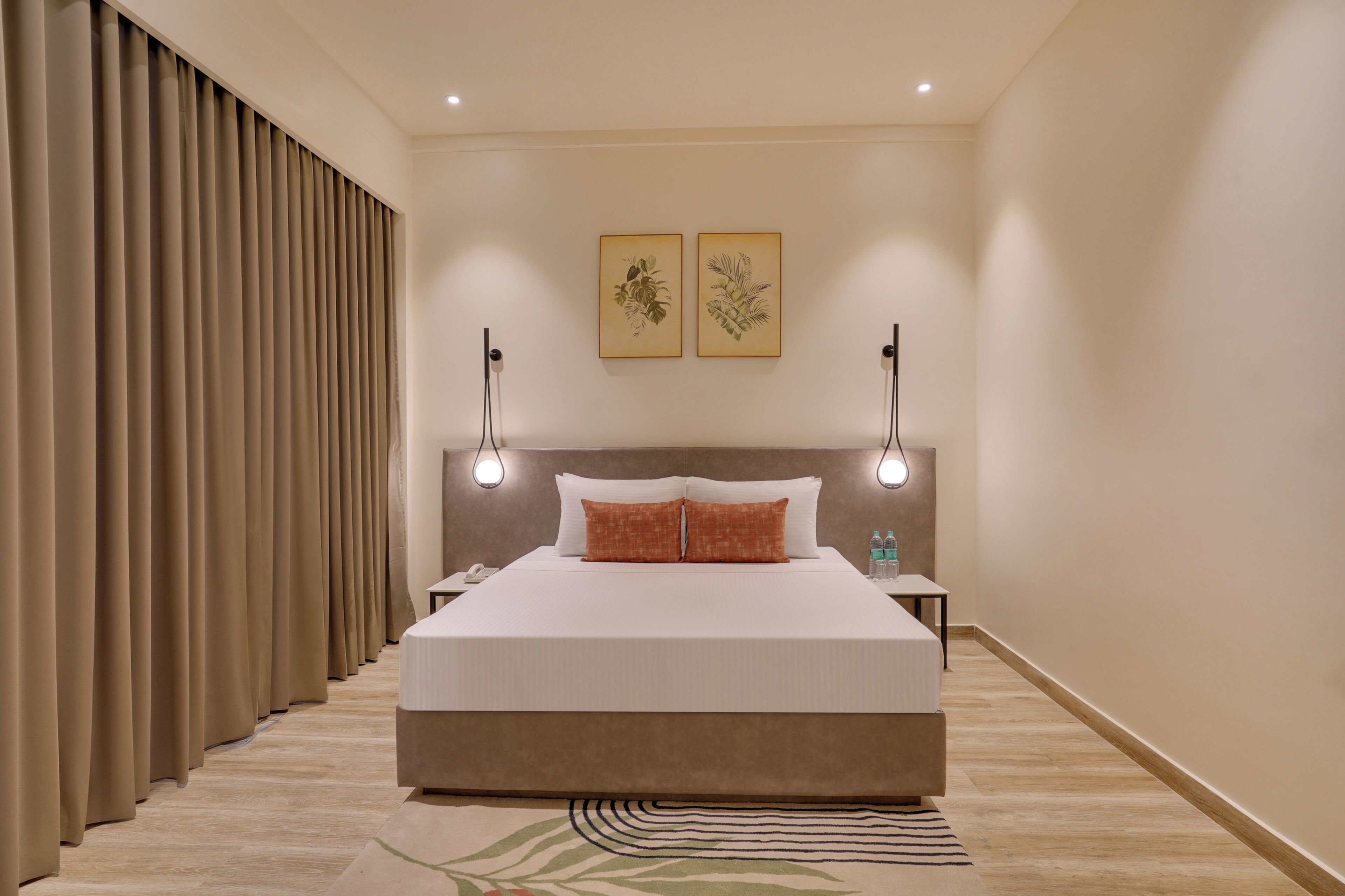 A hotel room with a large bed, two wall-mounted lamps, a nightstand, a bedside table, and a large window with blinds.