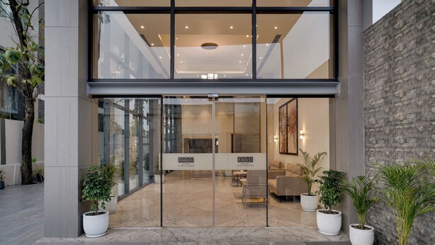 Una entrada moderna a un edificio con puertas de cristal, asientos interiores y plantas en macetas.