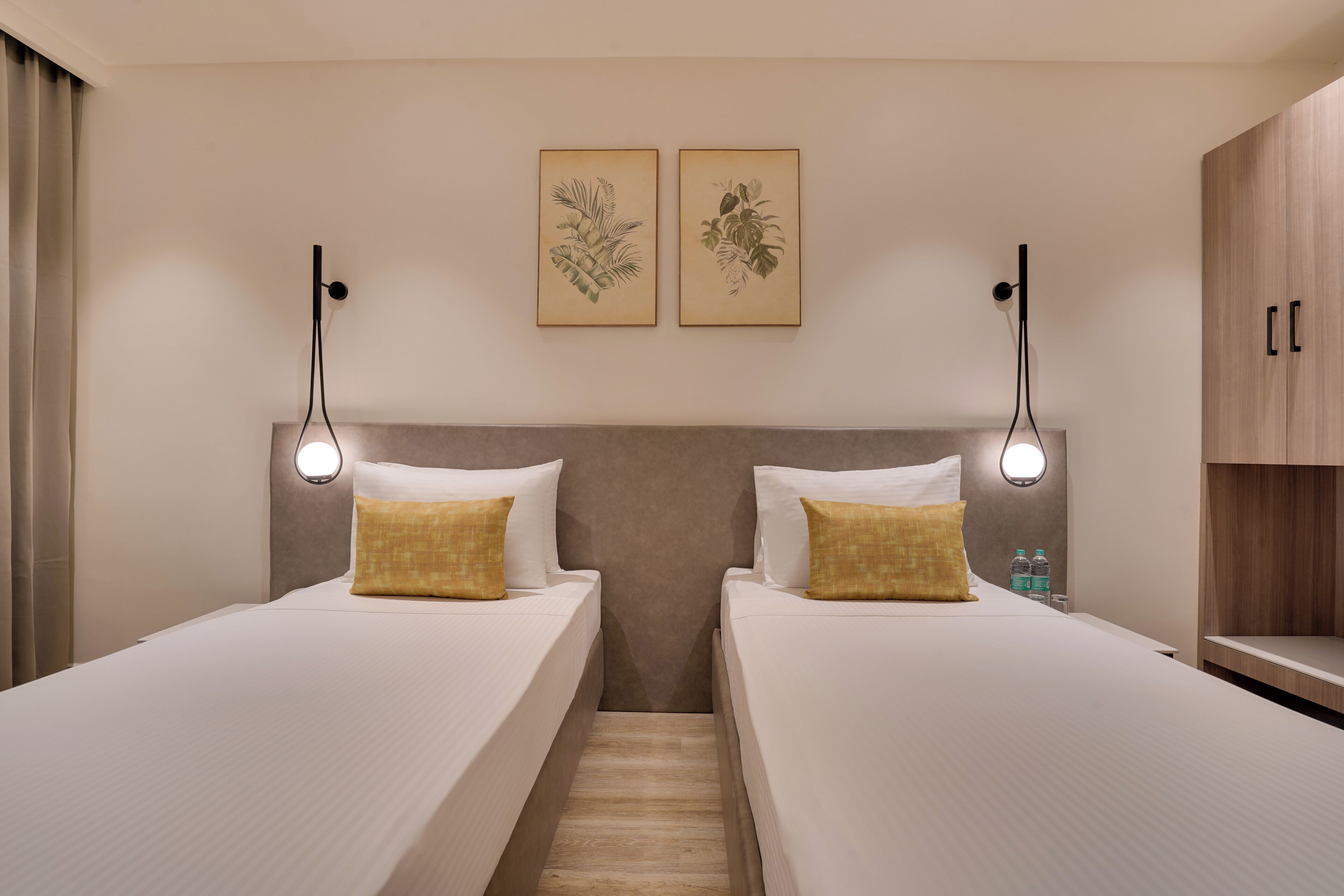 A hotel room with two beds, a headboard, wall-mounted artwork, bedside lamps, and a wooden cabinet.